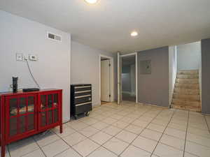 Empty room with a textured ceiling, electric panel, stairs, recessed lighting, and light tile patterned flooring