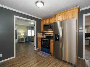 Kitchen with appliances with stainless steel finishes, ornamental molding, dark wood-style flooring, a textured ceiling, and dark countertops