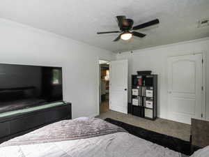Bedroom featuring carpet flooring, a textured ceiling, crown molding, and ceiling fan