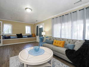 Living area with ornamental molding, wood finished floors, healthy amount of natural light, and a textured ceiling