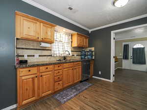 Kitchen featuring decorative backsplash, dark wood-style flooring, stainless steel dishwasher, ornamental molding, and brown cabinets