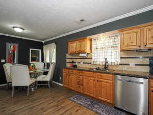 Kitchen featuring dishwasher, crown molding, dark wood-style flooring, dark stone countertops, and decorative backsplash