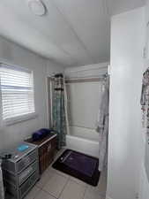 Full bathroom featuring shower / bath combo with shower curtain, a textured ceiling, and light tile patterned floors