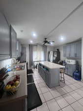 Kitchen featuring gray cabinetry, a kitchen bar, a center island, light tile patterned floors, and white appliances