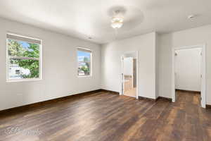 Unfurnished bedroom featuring dark wood-type flooring, a textured ceiling, ensuite bath, and ceiling fan