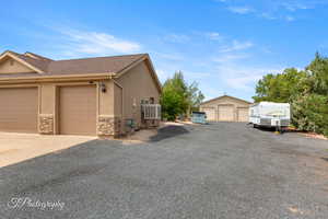 View of home's exterior featuring stucco siding, stone siding, a shingled roof, an outdoor structure, and a garage