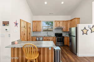 Kitchen with a peninsula, appliances with stainless steel finishes, tasteful backsplash, dark wood-style floors, and lofted ceiling