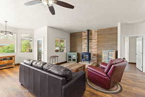 Living area featuring wooden walls, a wood stove, wood finished floors, a textured ceiling, and a ceiling fan