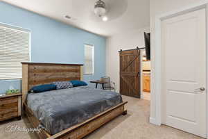 Bedroom featuring light colored carpet, a barn door, and ensuite bath