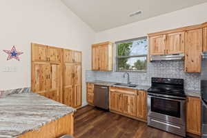 Kitchen with appliances with stainless steel finishes, light stone counters, lofted ceiling, tasteful backsplash, and dark wood-type flooring