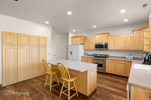 Kitchen featuring light brown cabinetry, a kitchen bar, stainless steel appliances, dark wood-style flooring, and recessed lighting