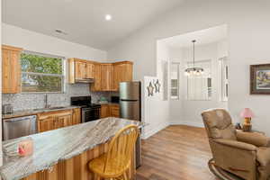 Kitchen featuring light stone counters, decorative backsplash, lofted ceiling, appliances with stainless steel finishes, and hanging light fixtures