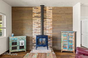 Detailed view of wood walls, a wood stove, wood finished floors, and a textured ceiling