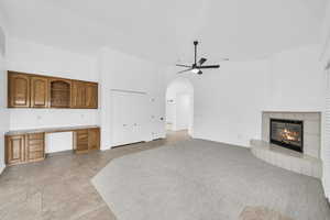 Unfurnished living room with built in desk, arched walkways, a tile fireplace, ceiling fan, and light stone finish flooring