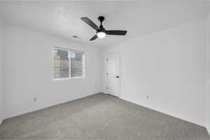 Carpeted empty room with a textured ceiling and ceiling fan