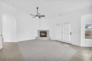 Unfurnished living room with a tile fireplace, a ceiling fan, arched walkways, and light stone finish floors