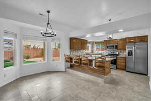 Kitchen featuring brown cabinetry, light stone counters, appliances with stainless steel finishes, decorative backsplash, and a peninsula