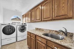 Laundry area with cabinet space, a textured ceiling, separate washer and dryer, and light tile patterned floors