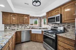 Kitchen featuring appliances with stainless steel finishes, decorative backsplash, brown cabinetry, light stone countertops, and recessed lighting