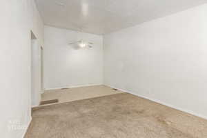 Spare room featuring light carpet, a textured ceiling, and a ceiling fan