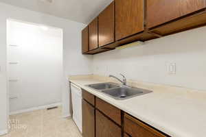 Kitchen featuring light countertops, white dishwasher, a textured ceiling, and light tile patterned floors
