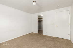 Unfurnished bedroom featuring carpet flooring, a walk in closet, and a textured ceiling