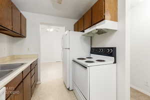 Kitchen featuring white appliances, a textured ceiling, light countertops, under cabinet range hood, and brown cabinetry