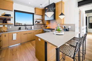 Kitchen with pendant lighting, open shelves, light wood-style flooring, a breakfast bar, and tasteful backsplash