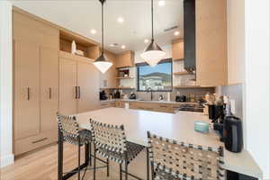Kitchen featuring hanging light fixtures, light countertops, a peninsula, open shelves, and a breakfast bar