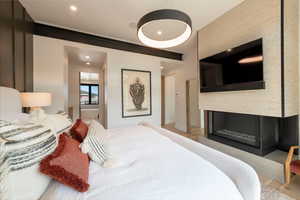 Bedroom featuring a glass covered fireplace, light wood-style floors, recessed lighting, and connected bathroom