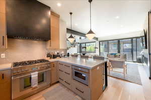Kitchen featuring stainless steel range, exhaust hood, tasteful backsplash, pendant lighting, and light wood-style flooring