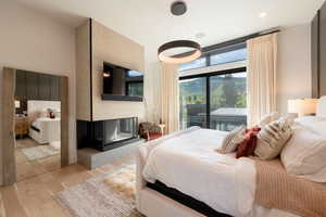Bedroom featuring wood finished floors, a multi sided fireplace, and access to exterior