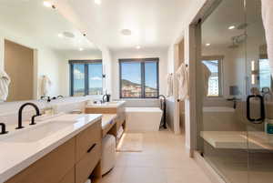 Full bathroom featuring two vanities, a shower stall, light tile patterned floors, a freestanding bath, and recessed lighting