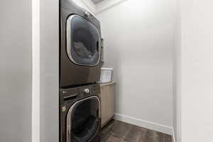 Laundry room with stacked washing machine and dryer, cabinet space, and dark tile patterned flooring