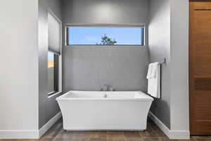 Full bathroom featuring a soaking tub, plenty of natural light, a textured wall, and dark tile patterned floors