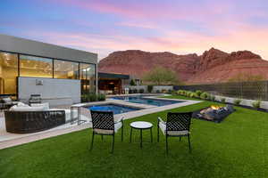 Pool at dusk with an outdoor living space with a fire pit, a patio, a fenced backyard, a mountain view, and a pool with connected hot tub