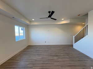 Unfurnished room featuring a raised ceiling, dark wood-style flooring, ceiling fan, stairway, and recessed lighting