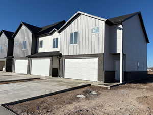 View of front of house with brick siding, an attached garage, concrete driveway, and board and batten siding