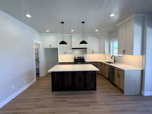 Kitchen featuring a center island, appliances with stainless steel finishes, decorative light fixtures, dark wood-type flooring, and white cabinetry