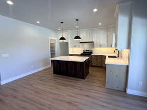 Kitchen featuring decorative backsplash, gas range, a kitchen island, white cabinetry, and dark brown cabinetry