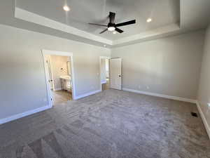 Unfurnished bedroom with a tray ceiling, light carpet, a ceiling fan, connected bathroom, and recessed lighting