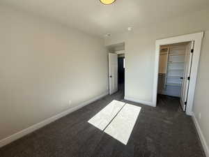 Unfurnished bedroom featuring dark carpet and a walk in closet