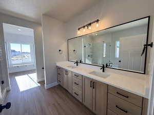 Bathroom featuring a shower stall, double vanity, light wood-style flooring, and a textured ceiling