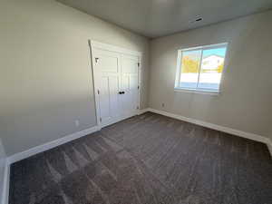 Unfurnished bedroom featuring dark carpet and a closet
