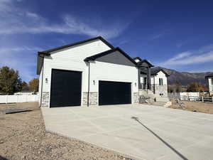 View of property exterior with a garage, stone siding, a mountain view, and concrete driveway