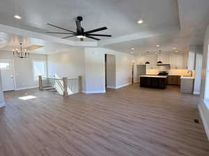 Unfurnished living room with recessed lighting, a tray ceiling, light wood finished floors, ceiling fan, and a chandelier