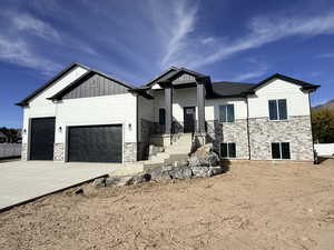 View of front of house featuring stone siding, a garage, concrete driveway, and board and batten siding