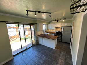 Kitchen with ornamental molding, freestanding refrigerator, stainless steel range with electric stovetop, white cabinetry, and a peninsula