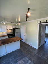 Kitchen featuring white cabinets, appliances with stainless steel finishes, tasteful backsplash, a peninsula, and wooden counters