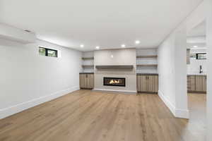 Basement living room featuring engineered wood flooring, recessed lighting, storage, and a fireplace.